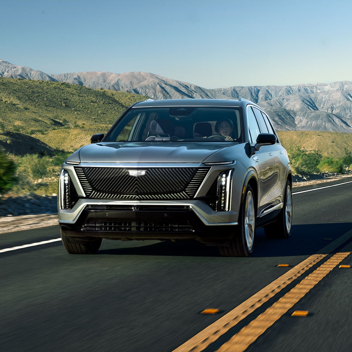 Le SUV électrique Cadillac VISTIQ 3 rangées 2027 roulant sur une route en montagne.