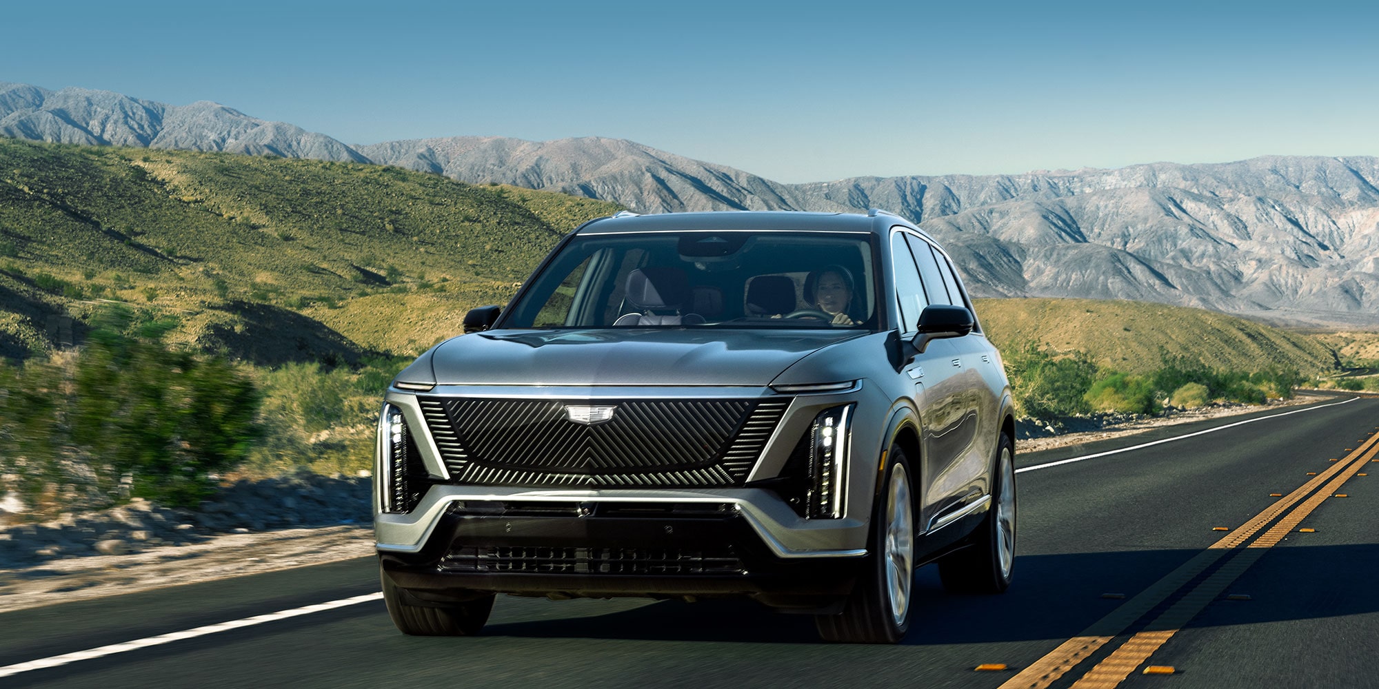 The Cadillac VISTIQ 3-row Electric SUV Driving Down a Road in the Mountains.