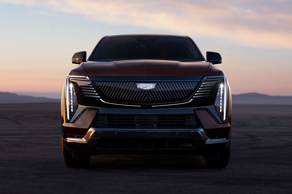 Front view of a Cadillac Escalade IQ electric SUV parked on an open landscape at sunset.