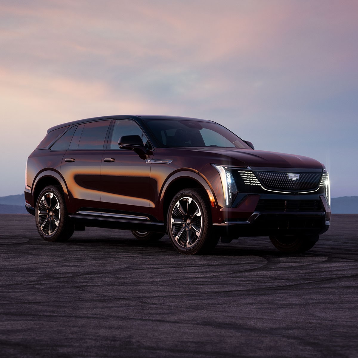 Front three-quarter view of a Cadillac Escalade IQ electric SUV parked on an open landscape at sunset.
