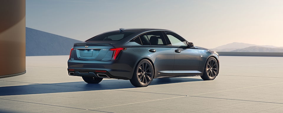 Rear-side view of the 2025 Cadillac CT5 sedan parked solitarily near the mountains.