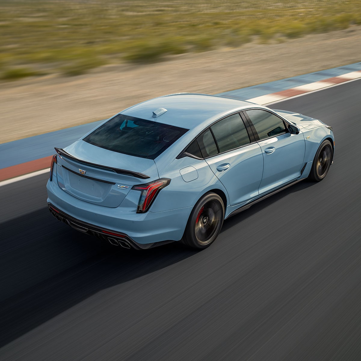 Vue latérale arrière de la Cadillac CT5-V 2025 en mouvement sur une route de campagne.