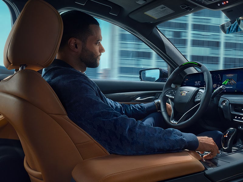 Vue côté passager d'un homme conduisant une Cadillac utilisant la technologie mains libres Super Cruise