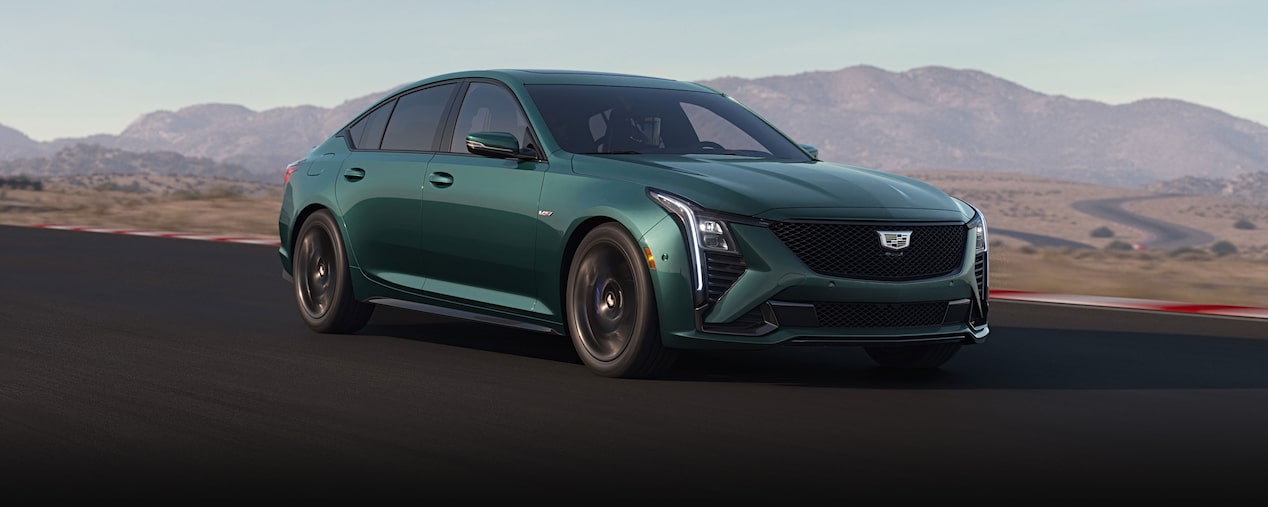 Vue latérale d'une Cadillac CT5-V bleu clair roulant sur une route avec des montagnes visibles au loin.
