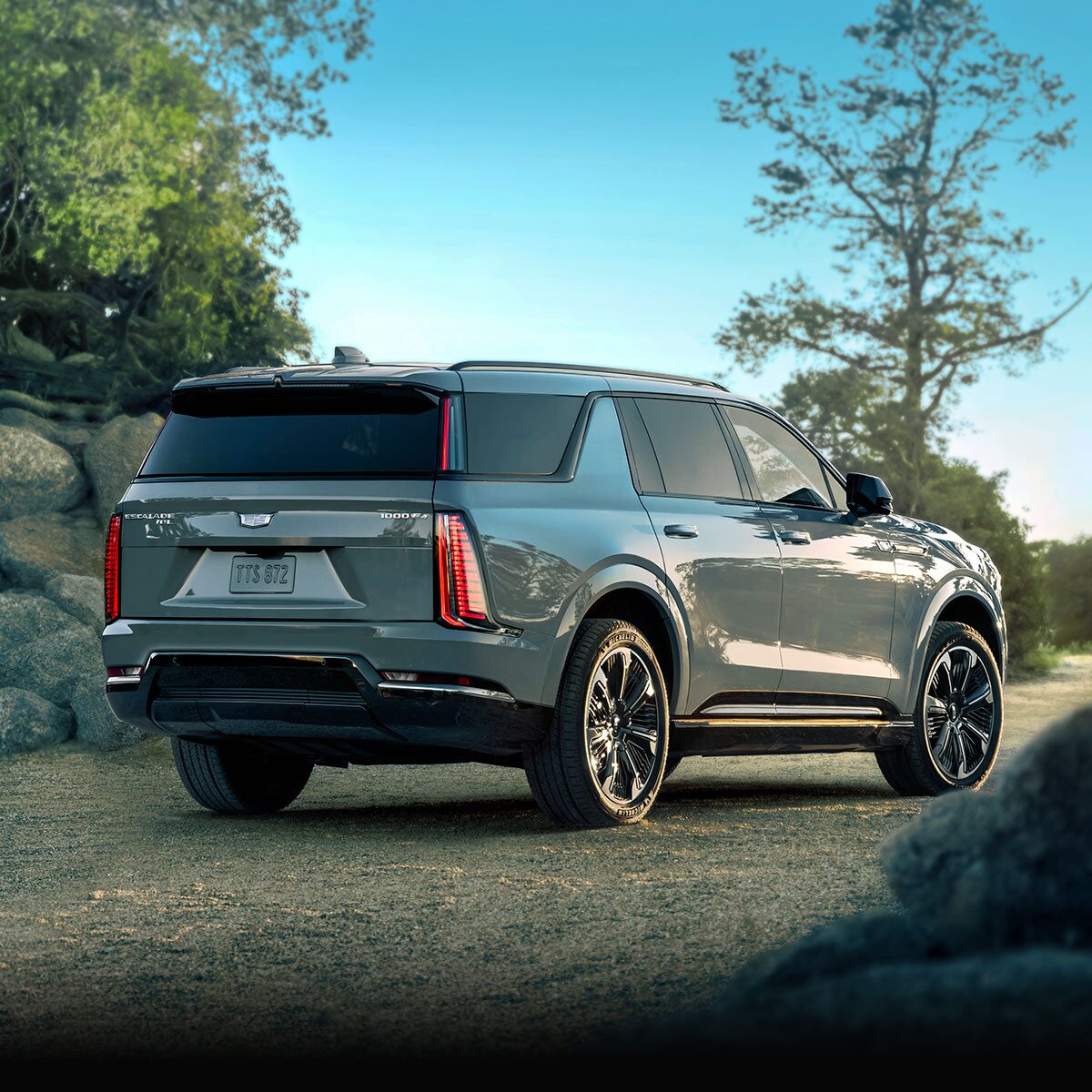 Rear Three-quarter View of the 2026 ESCALADE IQL Parked near a Rocky Trail