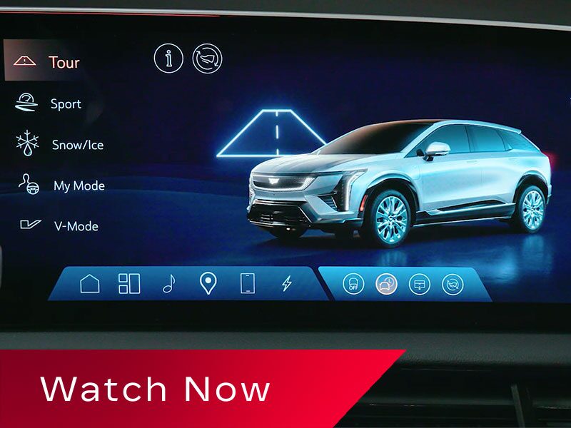 A Cadillac OPTIQ Infotainment Screen Displaying Drive Mode Options Beside a Rendered Image Of a Silver Cadillac SUV Above a Red Banner Reading “Watch Now.”
