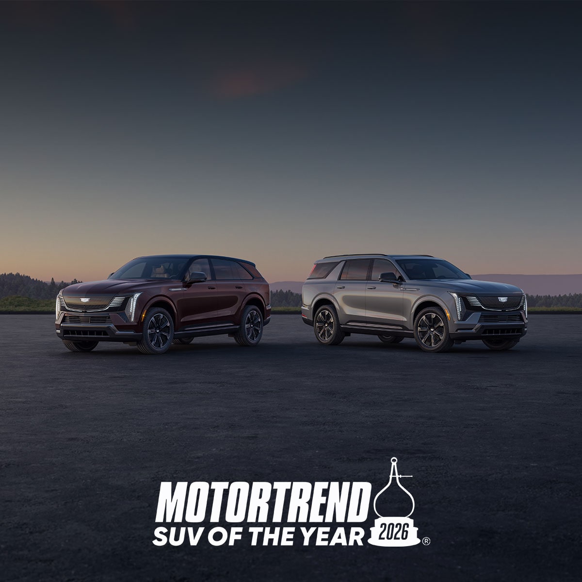 A Pair Of 2026 Cadillac Escalade IQ And IQL SUVs Are Parked On An Open Paved Surface At Sunset Above A Large MotorTrend SUV Of The Year 2026 Logo