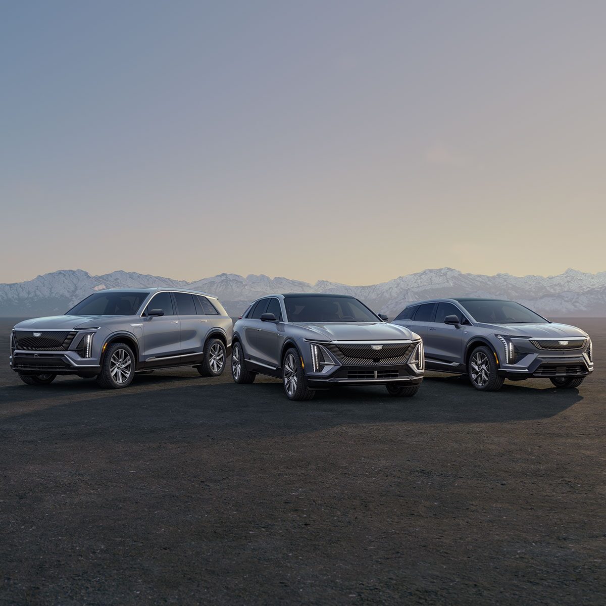 Three Cadillac Silver SUVs Parked on an Open Plain at Sunrise with  Mountains in the Background