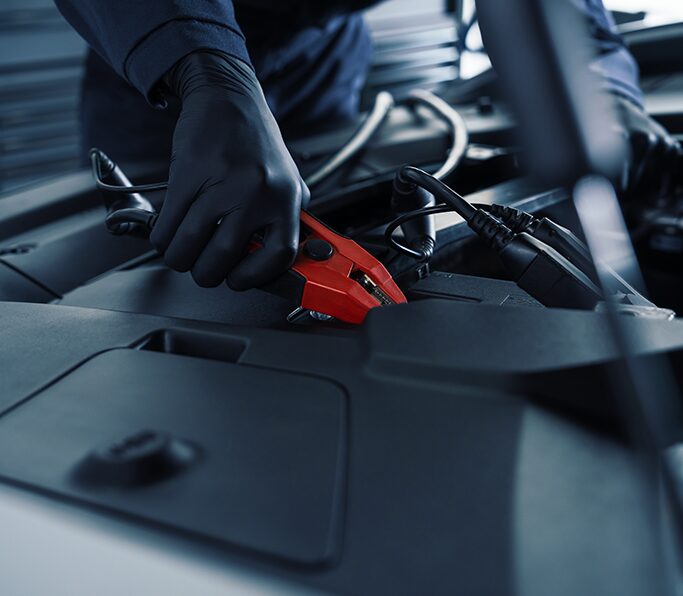Cadillac Certified Service Technician Attaching Jumper Cables on a Vehicle