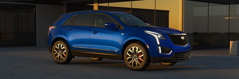 Three-quarters Passenger Side View of the a Blue 2025 Cadillac XT5 Parked Outside an Industrial Building