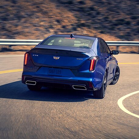 Rear End View of a Blue Cadillac CT4 Driving Around the Curve of a Mountain Road