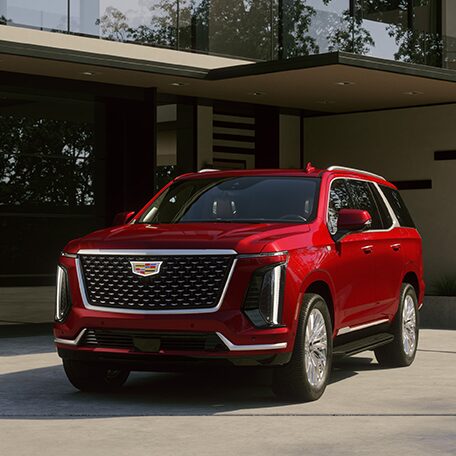 Three-quarter Driver's Side View of a Red Cadillac Escalade Parked Outside of a Modern Home