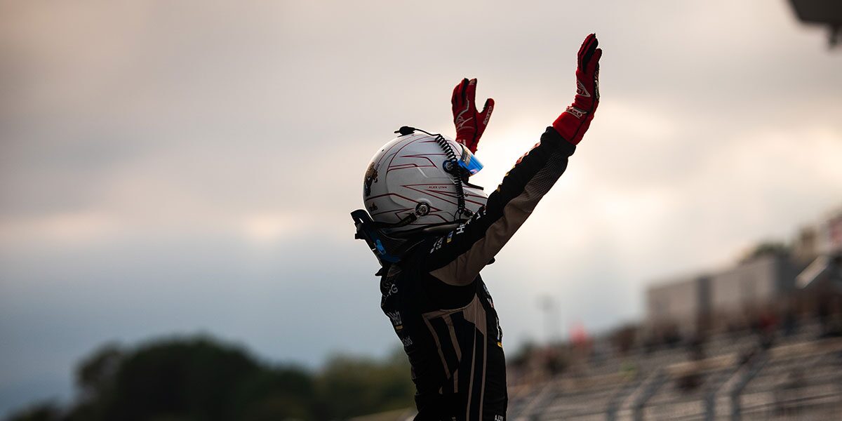Side View of a Race Car Driver Standing Up with Their Hands in the Air