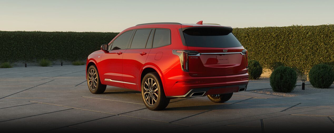 Rear Three-quarter View of a Red Cadillac XT6 Parked near a Grassy Wall