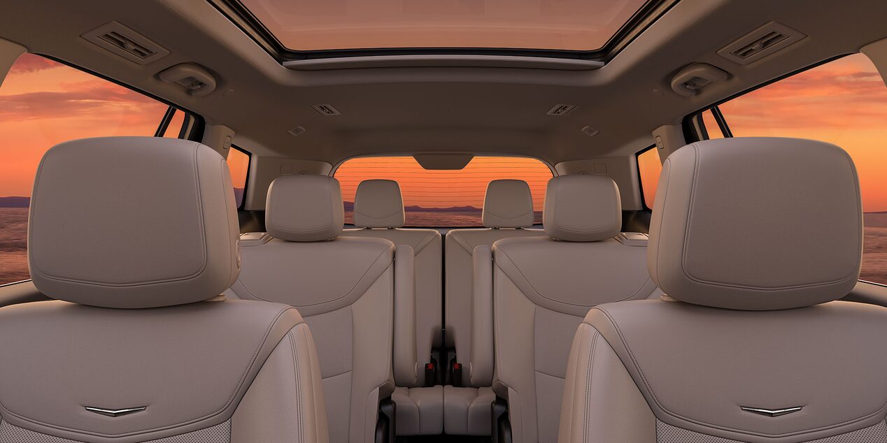 Three Rows of Tan Leather Seats Inside the New Cadillac XT6 Parked Under the Sunset