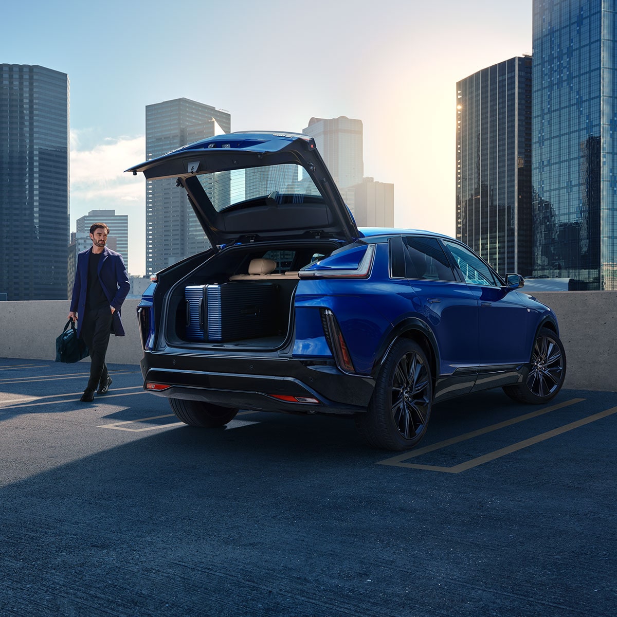 A Man Walking to an Opened Trunk of a Parked Blue 2025 Cadillac LYRIQ Overlooking the City