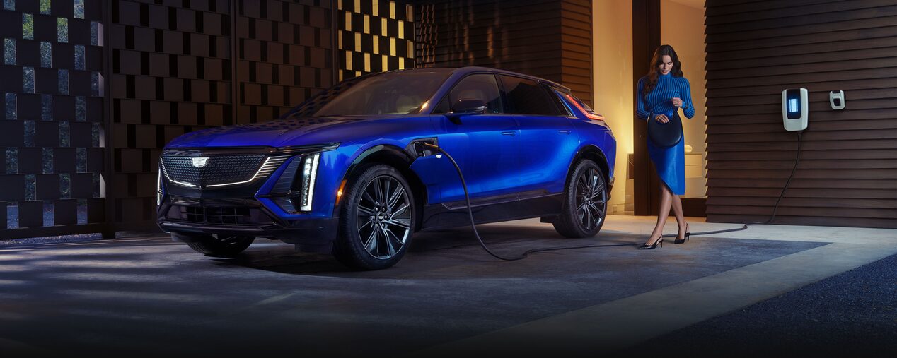 A Woman Looking in Her Purse Next to a Charging Blue Cadillac LYRIQ EV SUV