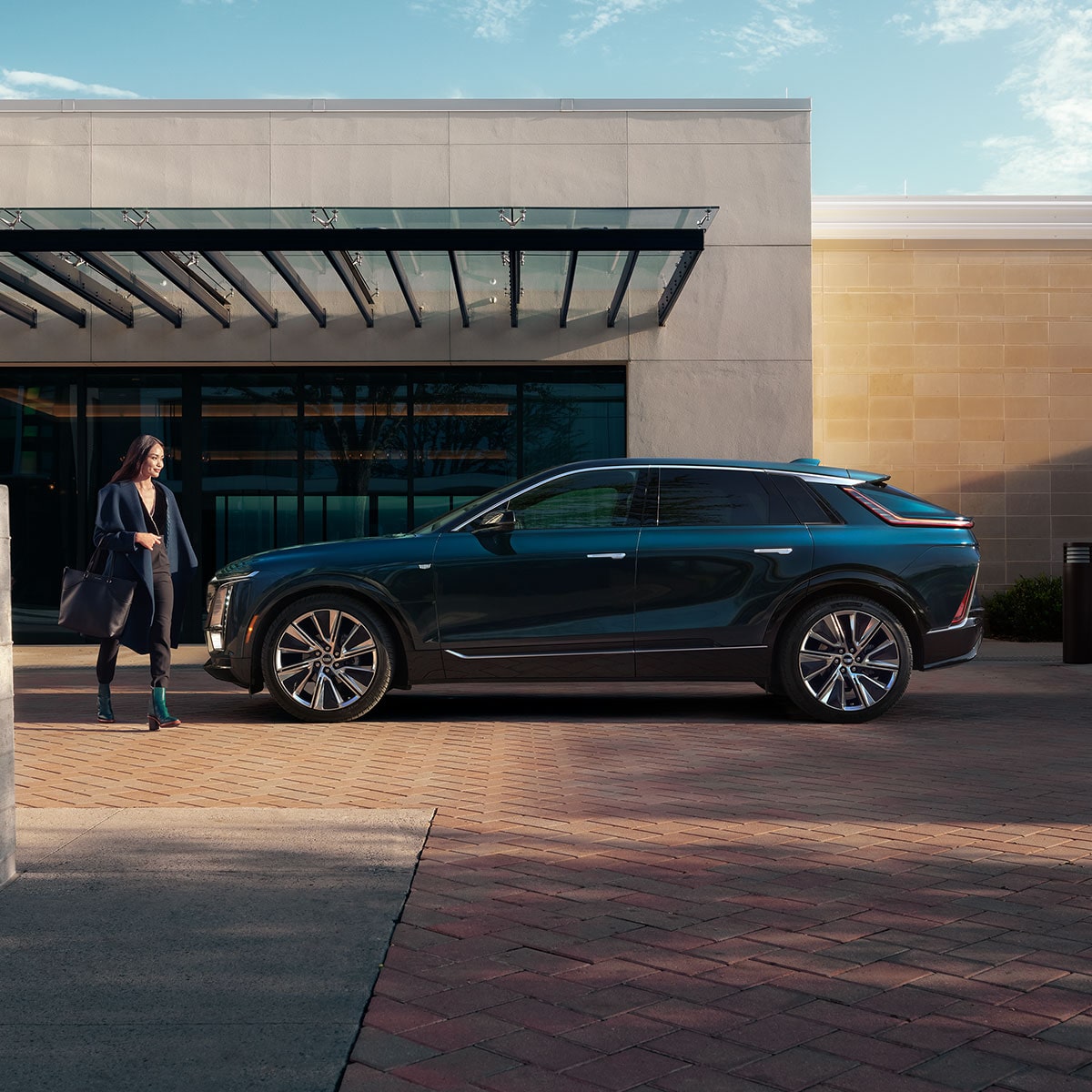 A Fashionably Dressed Woman Walks Toward a Parked Cadillac LYRIQ All-electric SUV