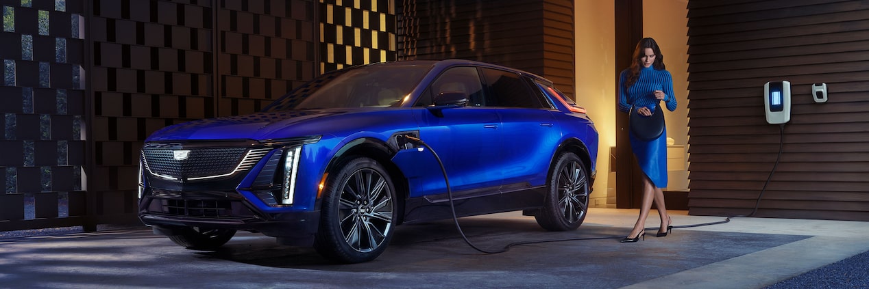 A Woman Looking in Her Purse Next to a Charging Blue Cadillac LYRIQ