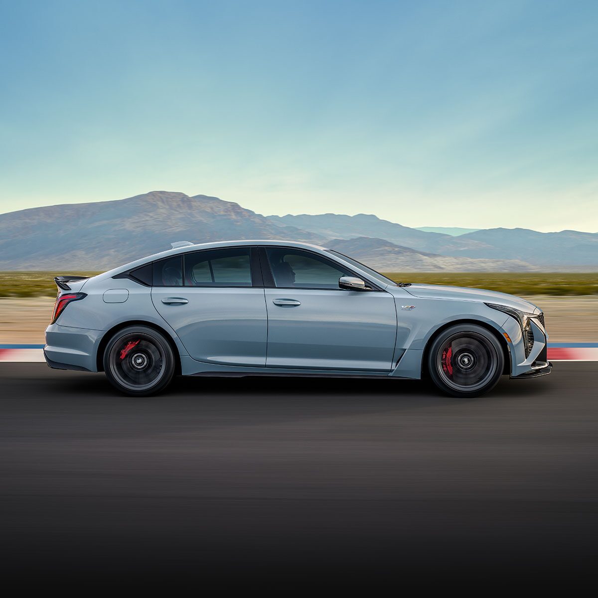 Side View of a Light Blue  Cadillac CT5-V Driving Down the Road with Mountains Visible in the Distance