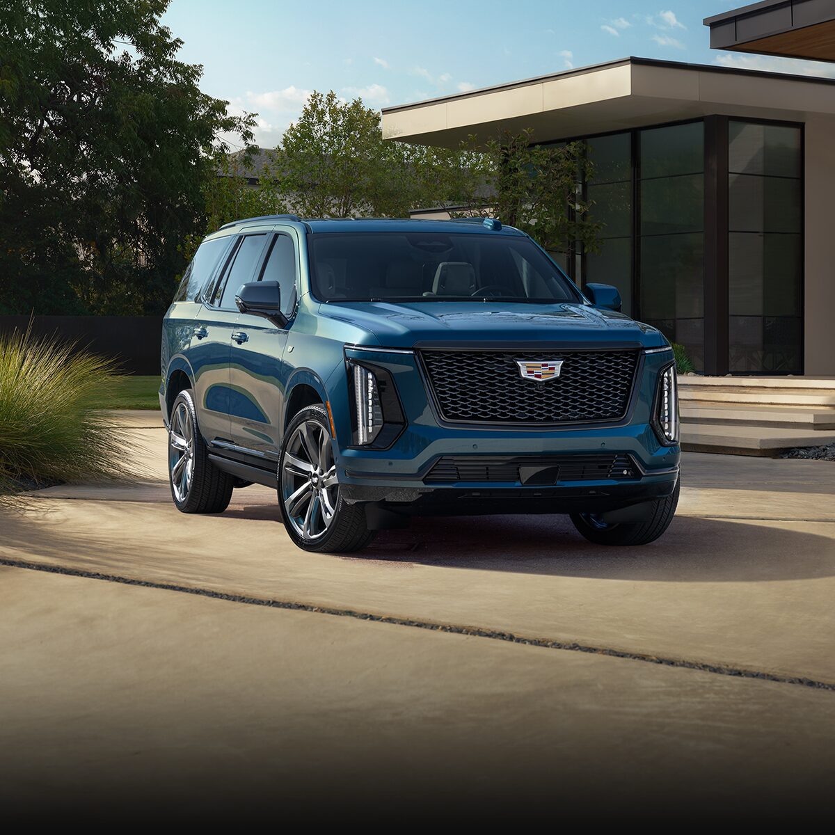 Three-Quarter View of a Blue 2026 Cadillac Escalade Parked in Front of a Modern Home