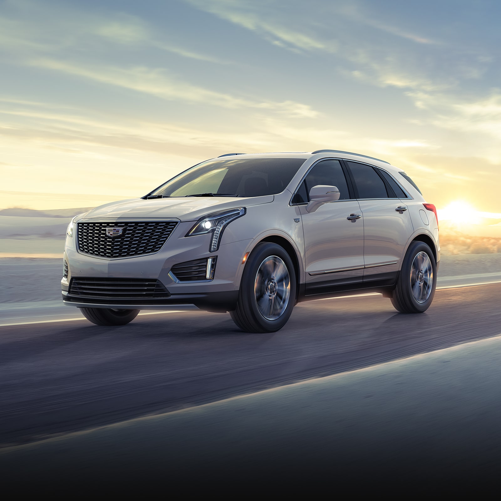 The 2026 Cadillac XT5 Driving on a Winding Road with Sun Rising in Background