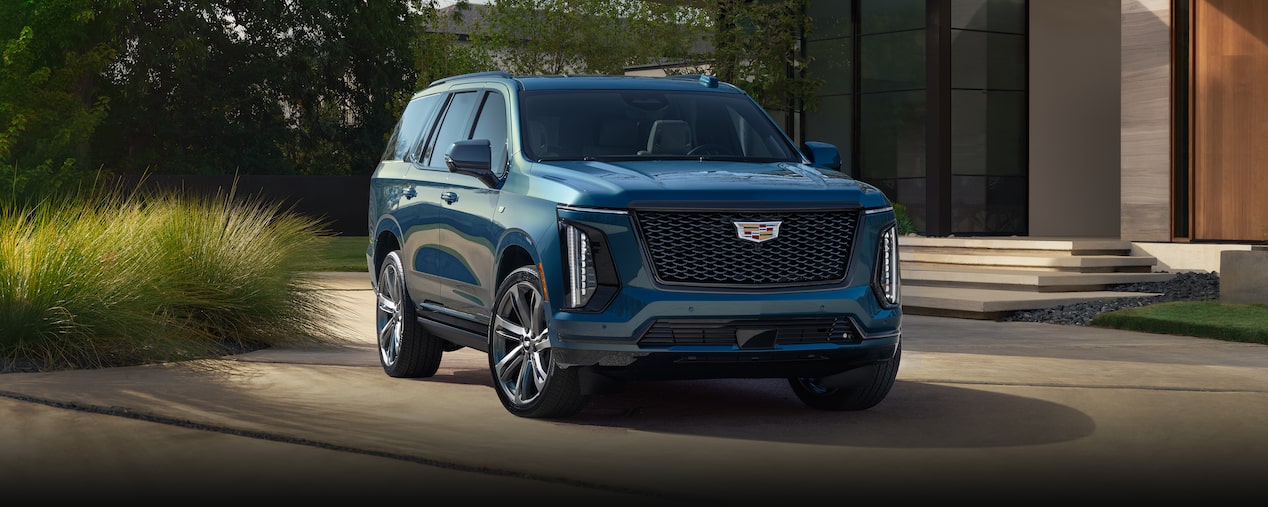 Three-Quarter View of a Blue 2025 Cadillac Escalade Parked in Front of a Modern Home