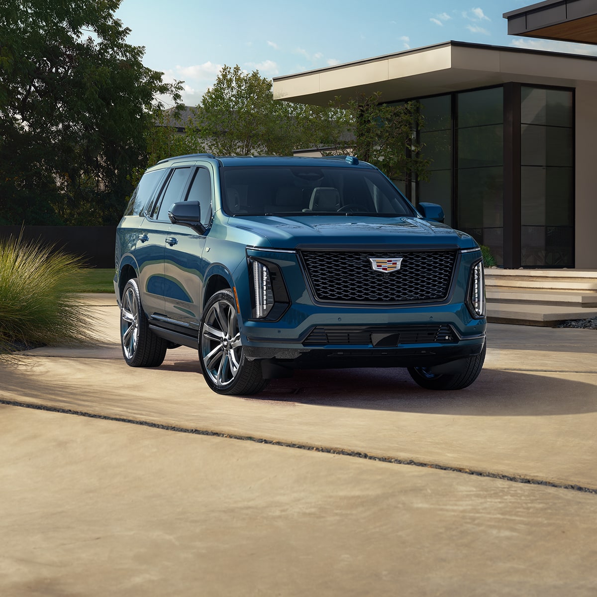 Three-Quarter View of a Blue 2025 Cadillac Escalade Parked in Front of a Modern Home