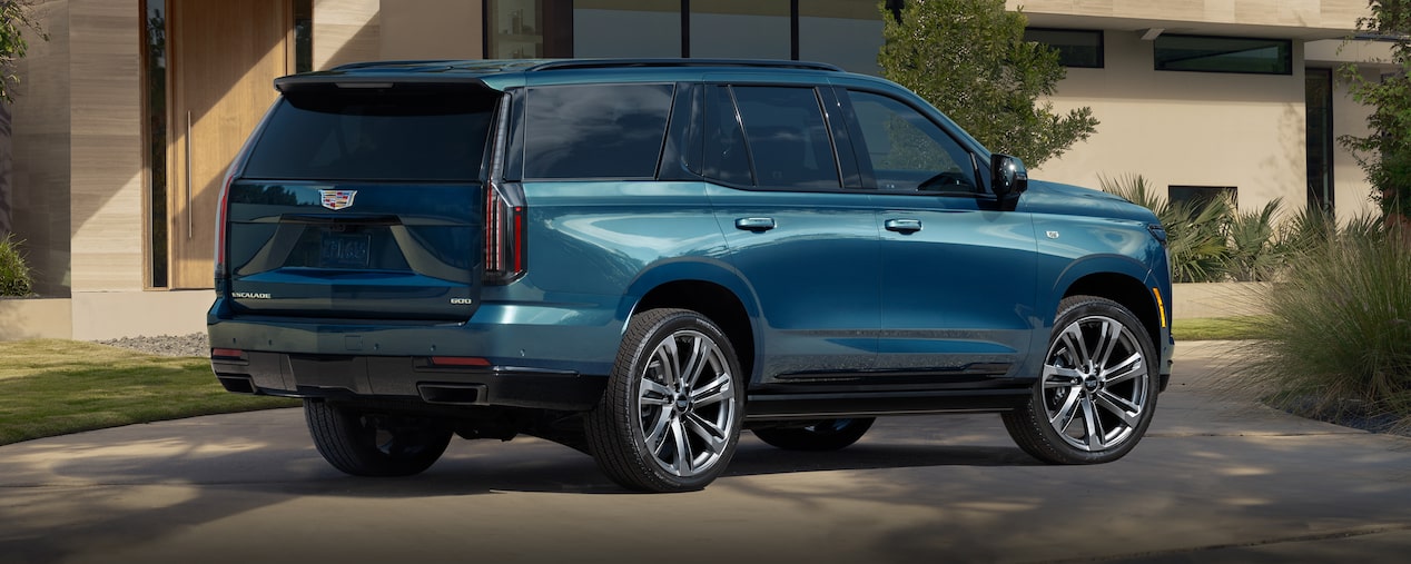 Three-Quarter Rear View of a Blue 2025 Cadillac Escalade Parked in Front of a Modern Home