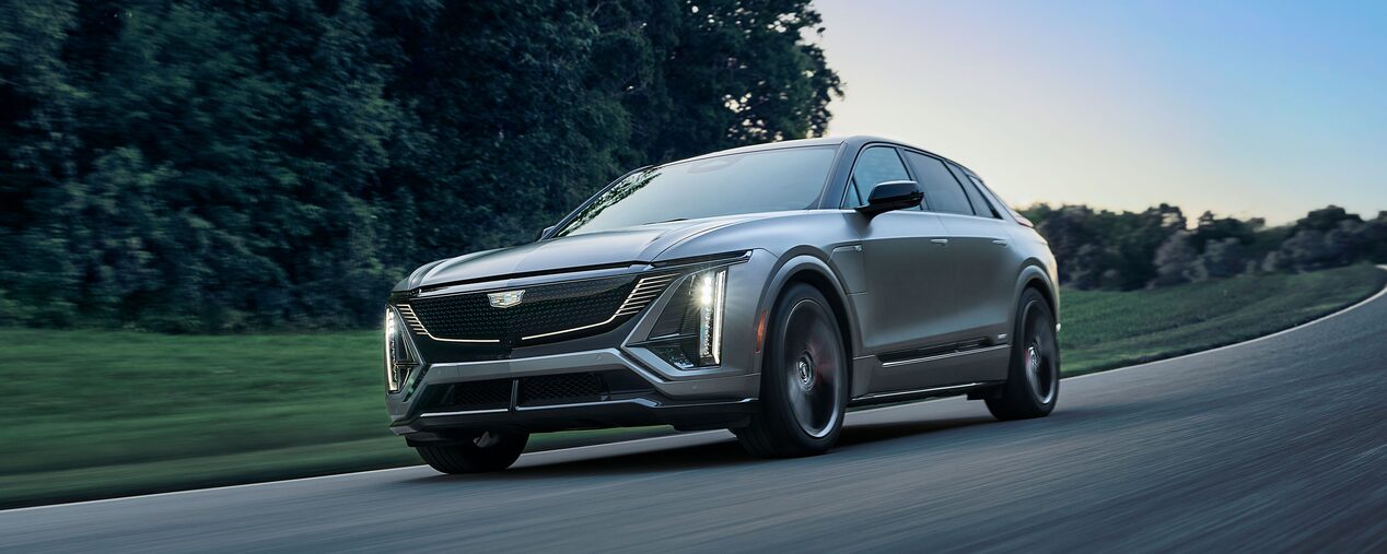 A Cadillac V-Series Vehicles Driving Around a Corner on a Road with Trees in the Background